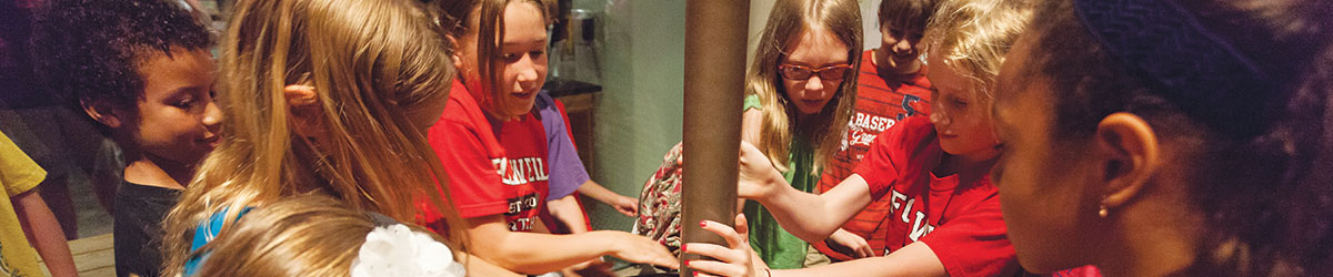 A group of kids gather around an interactive exhibit in the museum.