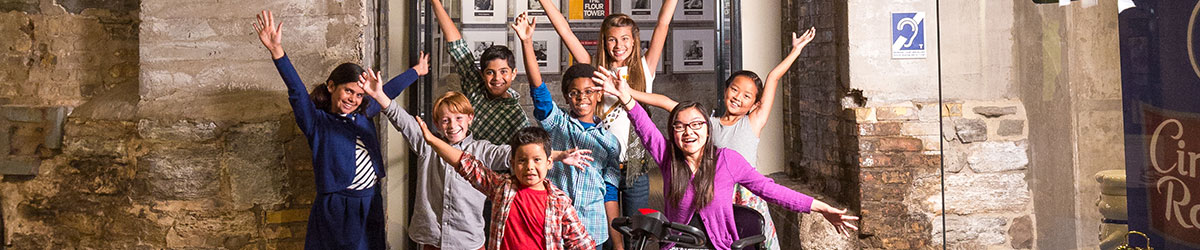 A group of children with arms raised standing in front of the entrance to the Flour Tower elevator exhibit.