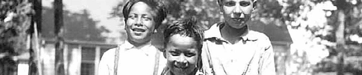 Black and white photo of three boys standing in front of a house.