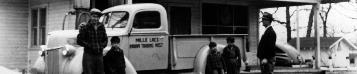 Black and white photo of three children and two grown-up standing in front of a truck.