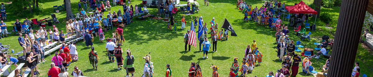Top view of an outside event with people dressed in traditional Ojibwe costumes.