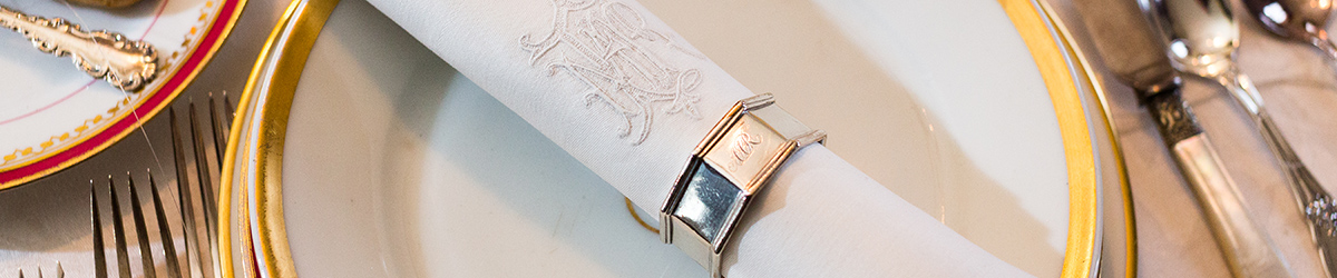 Place setting with cloth napkin with silver napkin ring resting on gold-edged plate