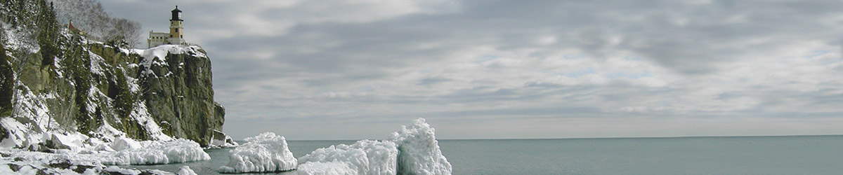 The lighthouse on a cliff at the top left, icy rocks in the foreground, ice-blue water and clouds to the right