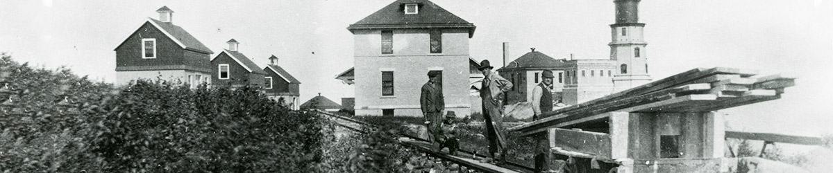 Men working on rail tracks with the lighthouse and several buildings in the background