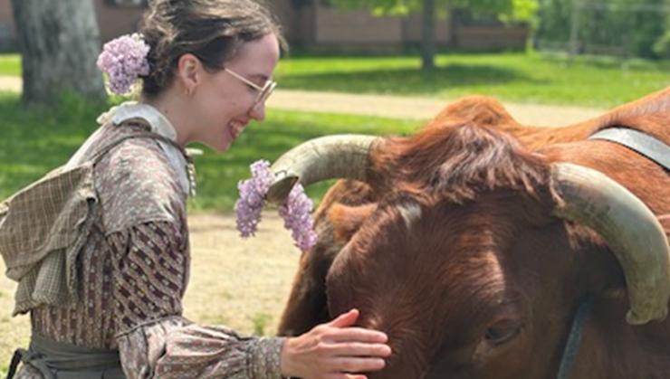 Woman in period clothes petting cow on a sunny spring day